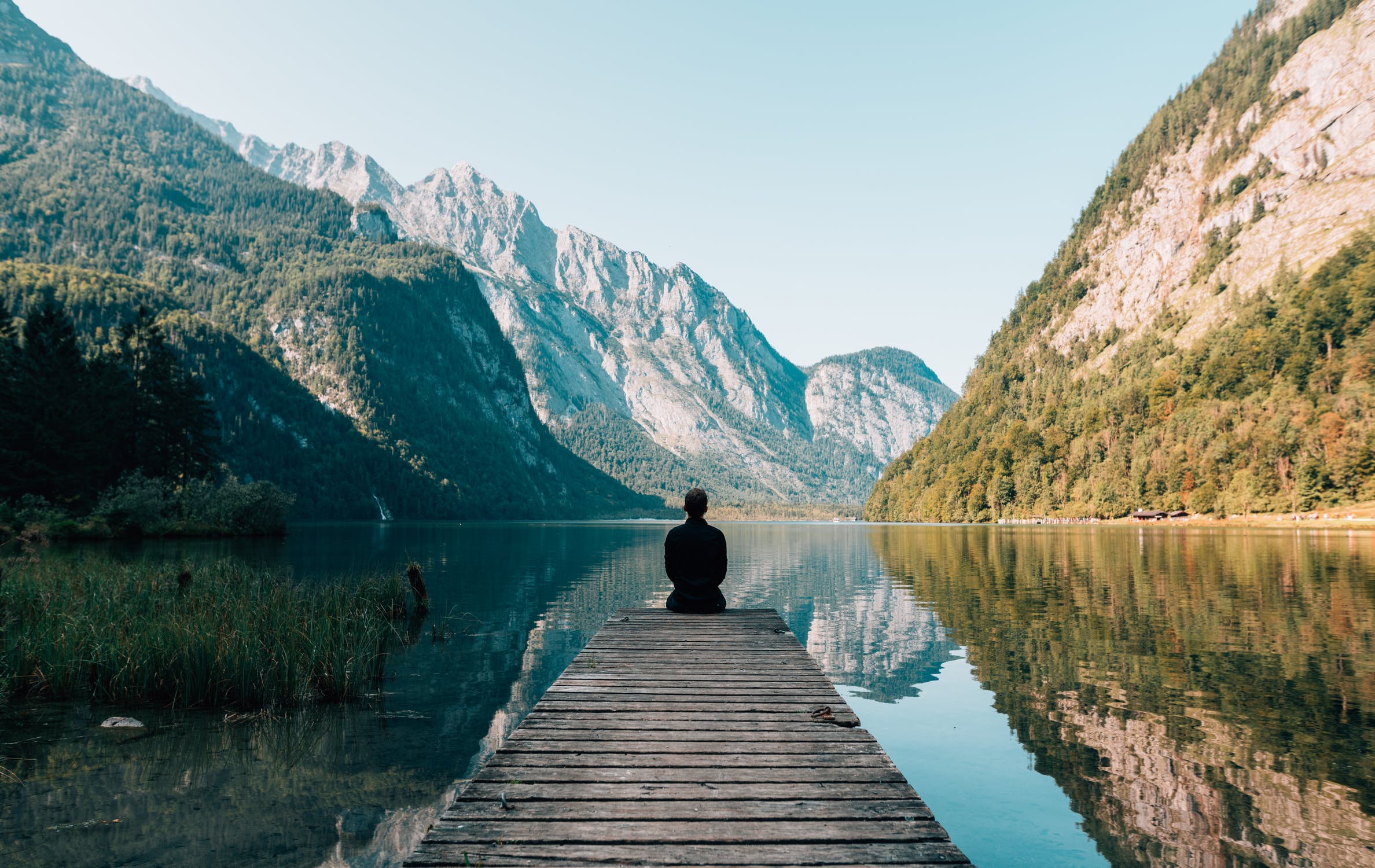 Person meditating on a dock by a mountain lake